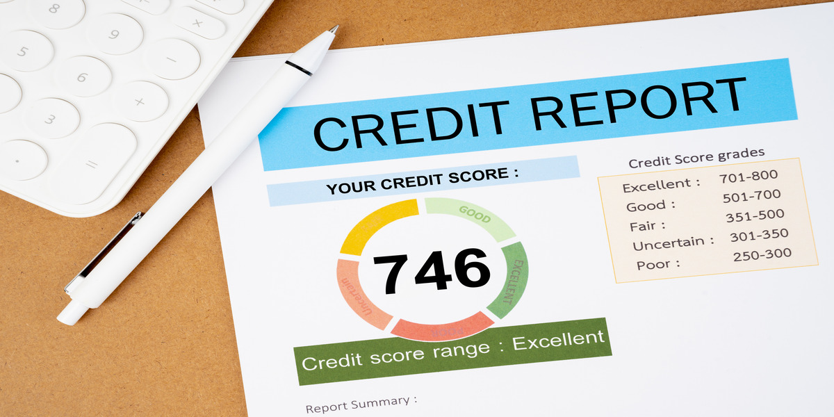 Close-up of a credit report displaying a score of 746 labeled as 'Excellent', alongside a breakdown of credit score grades ranging from 'Excellent' to 'Poor', with a white calculator and pen on a brown surface.