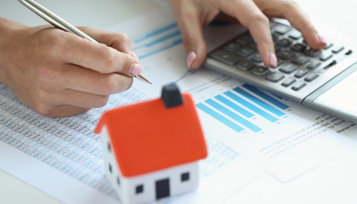Person working with a calculator with a model of a home on the desk. 