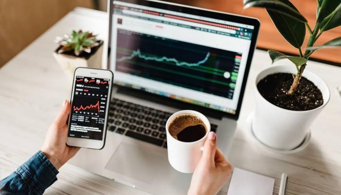 Analyzing stocks on a computer and cell phone with a coffee cup.