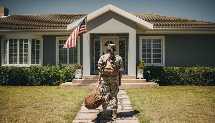 Veteran walks toward house with duffel bag in hand.