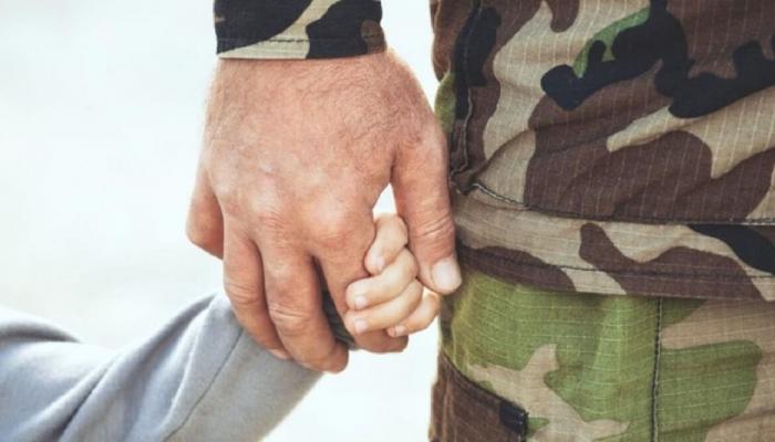 Close up of soldier holding hand with child.