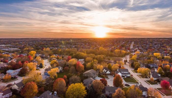 Aerial view of the sun setting over a suburban neighborhood with fall trees.  