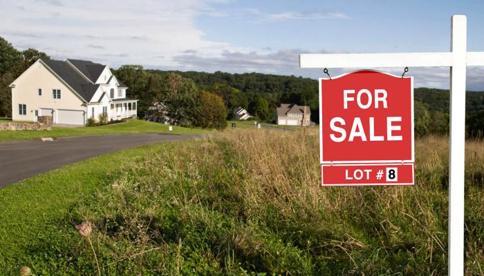 Red and white for sale sign in front of a large plot of land.