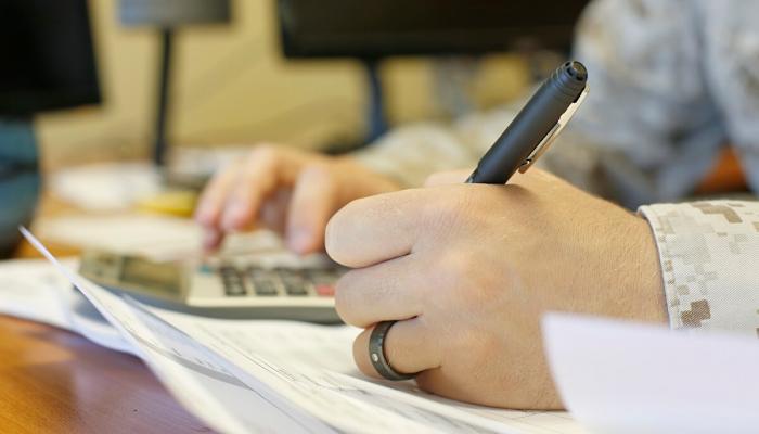 Close up of a mans hands doing paperwork and using a calculator.