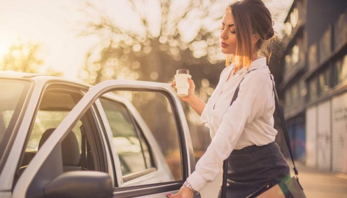 Woman holding coffee cup opens car door.