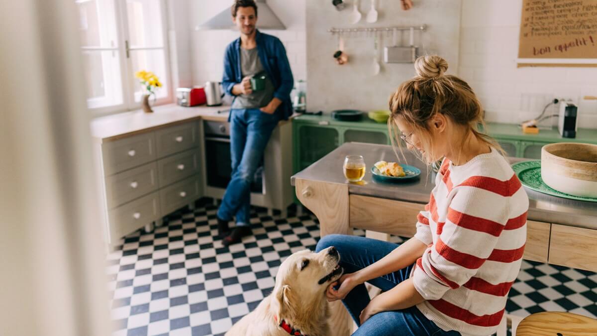 A couple in their kitchen with a dog. 