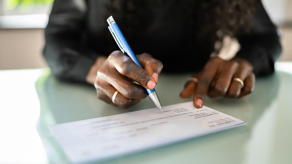 A woman's hands prepare to write on a check with a pen.
