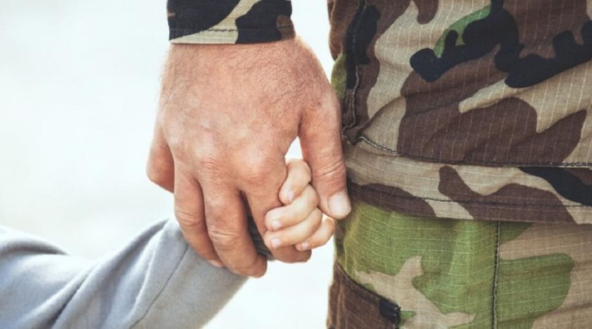 Close up of soldier holding hand with child.