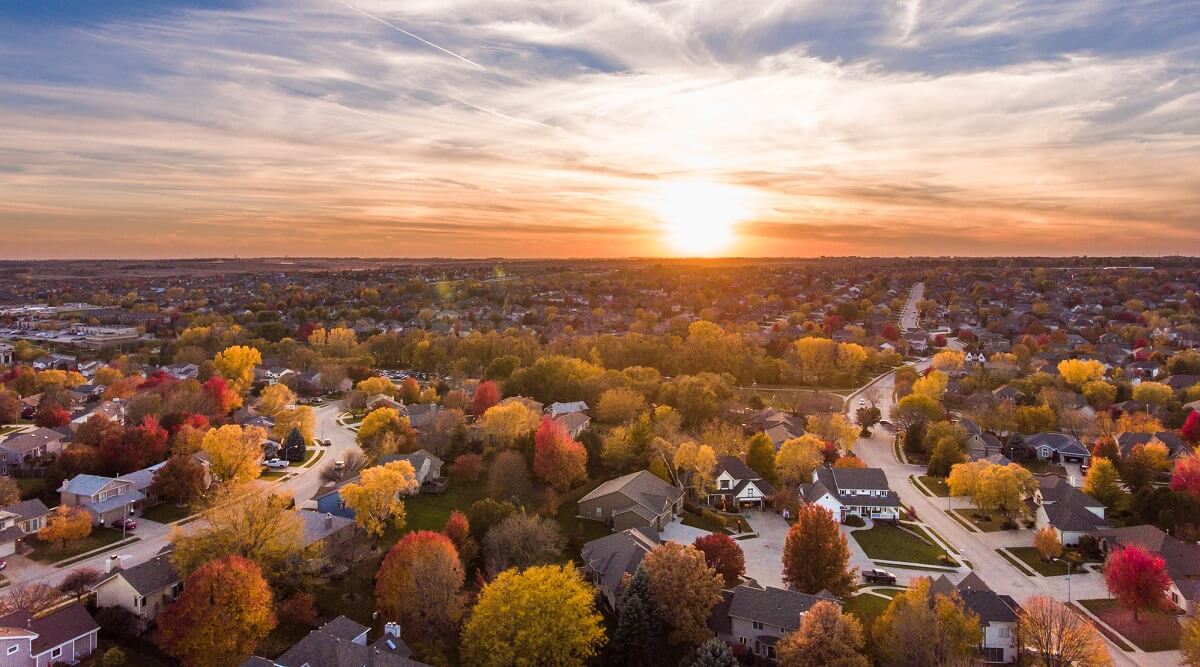 Aerial view of the sun setting over a suburban neighborhood with fall trees.  