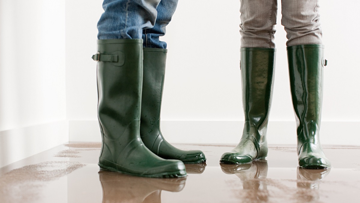 A couple wearing rainboots standing inside a flooded house.