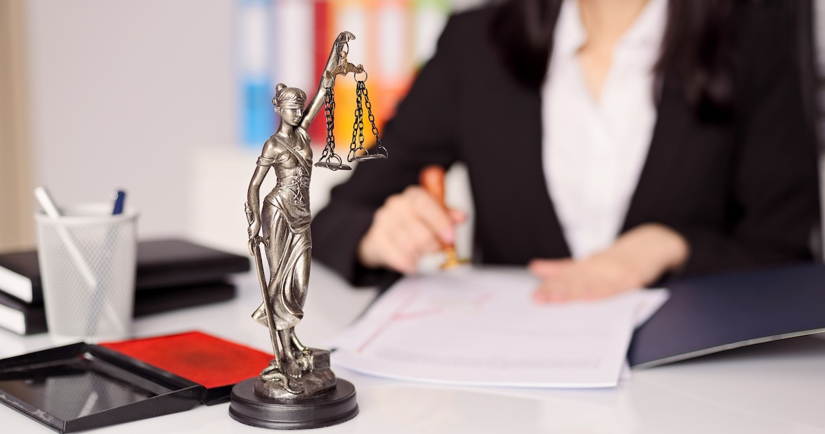 Small statue of goddess of justice on a lawyer's desk while she stamps a legal document.
