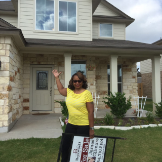 Arthenia T. stands in front of her new home holding the sold sign.