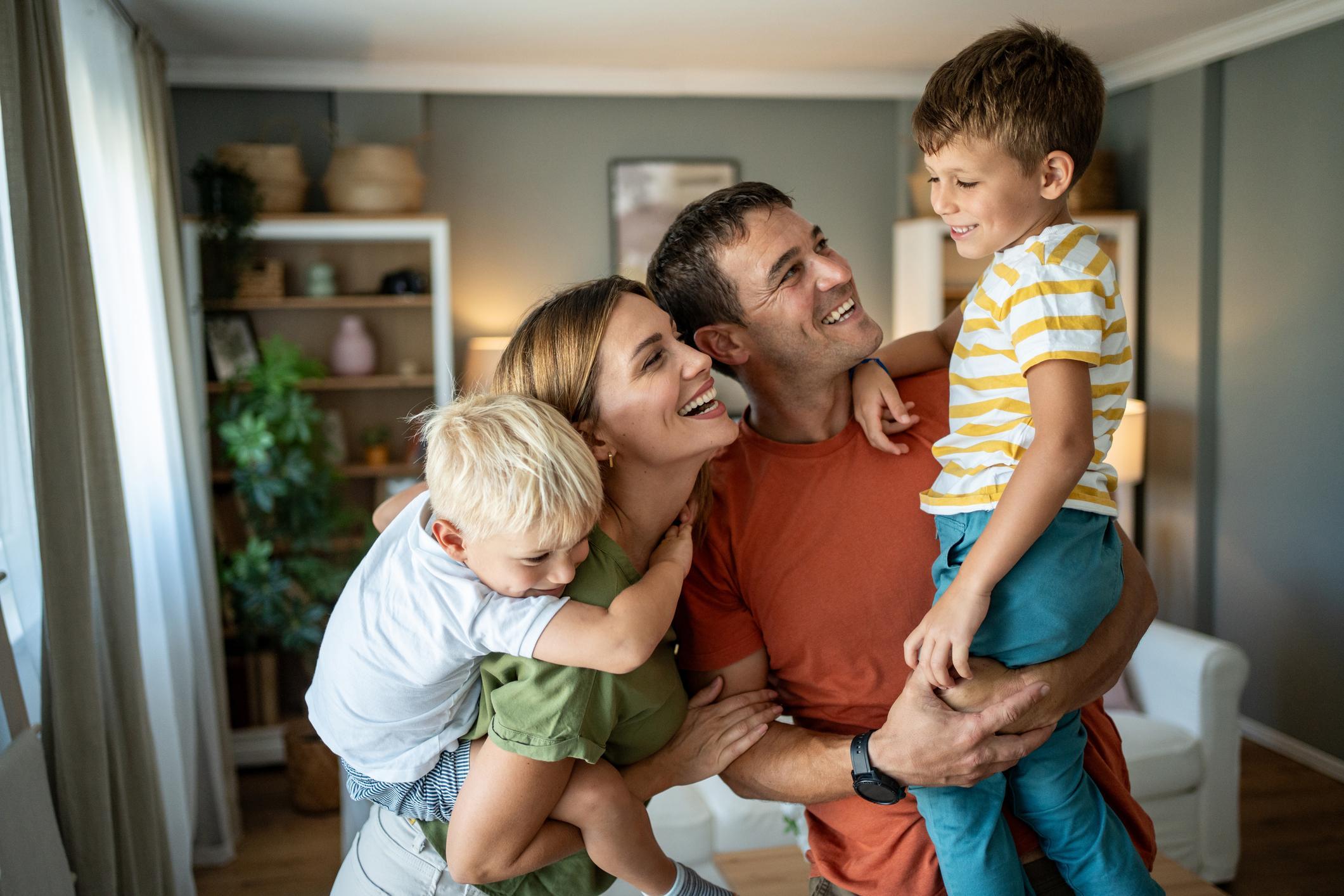 Cheerful parents joyfully carrying their two sons on their backs, creating playful moments and laughter together in the cozy living room.